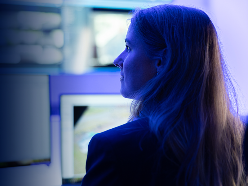Frau, die nach rechts schaut, vor mehreren Computerbildschirmen