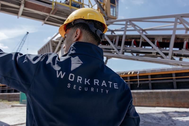 Workrate male security guard pointing on port site, photographed from behind