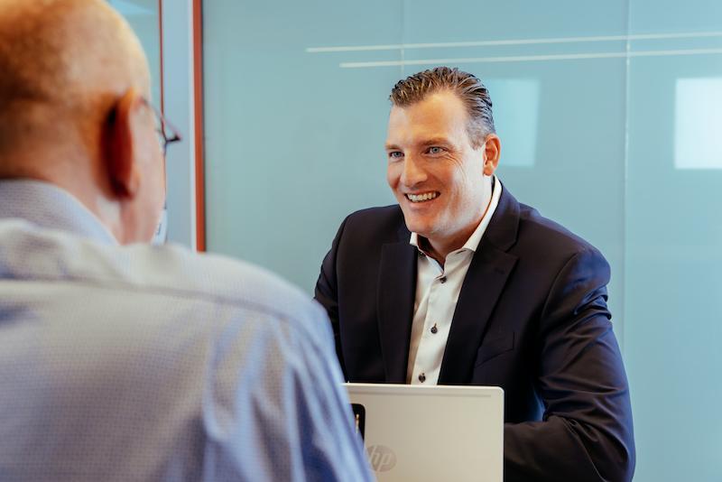 Man in a dark blue blazer with a white shirt smiling at his conversation partner.